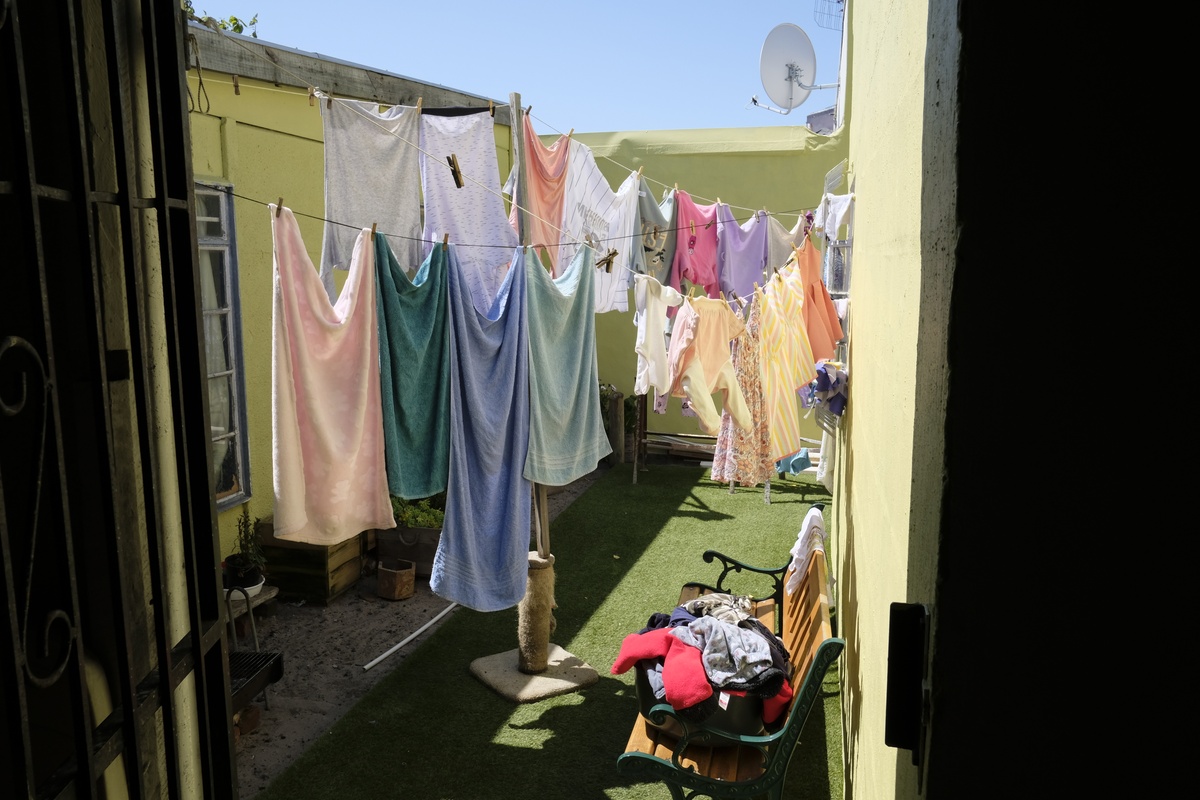 Process photograph from a visit to the Bonteheuwel township that formed part of ‘Open Production’, Igshaan Adams’ hybrid studio/exhibition in A4’s Gallery. A patio with concrete flooring and artificial grass plays host to clothing lines hung with variously coloured clothes.
