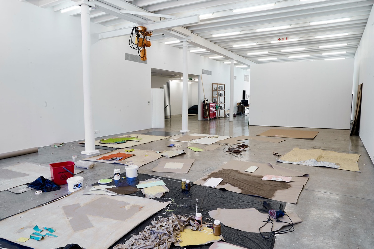 Process photograph of Asemahle Ntlonti’s working space during the 2nd rendition of ‘Parallel Play’ in A4’s Gallery. Sheets of black plastic, brown paper and art supplies line the gallery floor.
