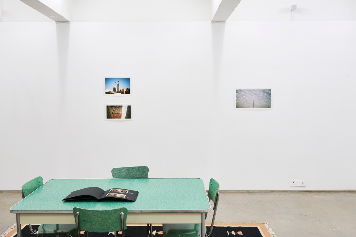 Installation photograph from the ‘Missing Subject’ exhibition in A4’s Library. At the front, a laminate table features a photo album of Andile Phewa’s photographs. On the left, Phewa’s photographs ‘Family Portrait’ and ‘Spy’ is mounted on the wall at the back. On the right, Phewa’s photograph ‘Nana’ is mounted on the wall at the back.
