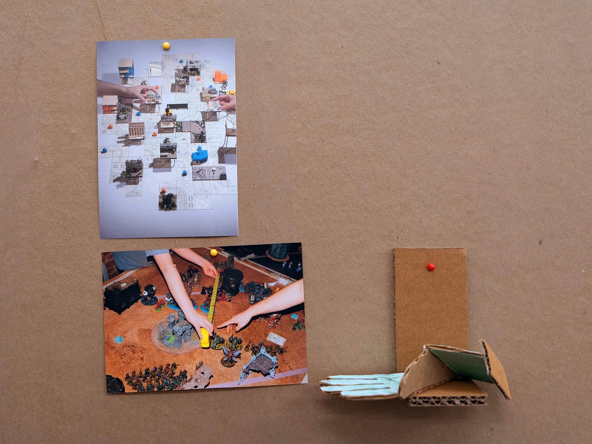 Installation photograph from Mitchell Gilbert Messina's residency in A4 Art Foundation shows a wall-mounted strip of cardboard hosting pinned research notes. The table-top as an arena for movement. Images of: (1) Siqi (Scott ) Chen’s _Reimagining the ‘Incompiuto Siciliano Archaeological Park’ _a two-player board game inspired by Carcassonne. (2) A player measuring range of motion in the table-top game _Warhammer_, taken from the NY Times article _Who’s Up for a Round of Warhammer_. (3) A sculpture of a glove made by the artist.
