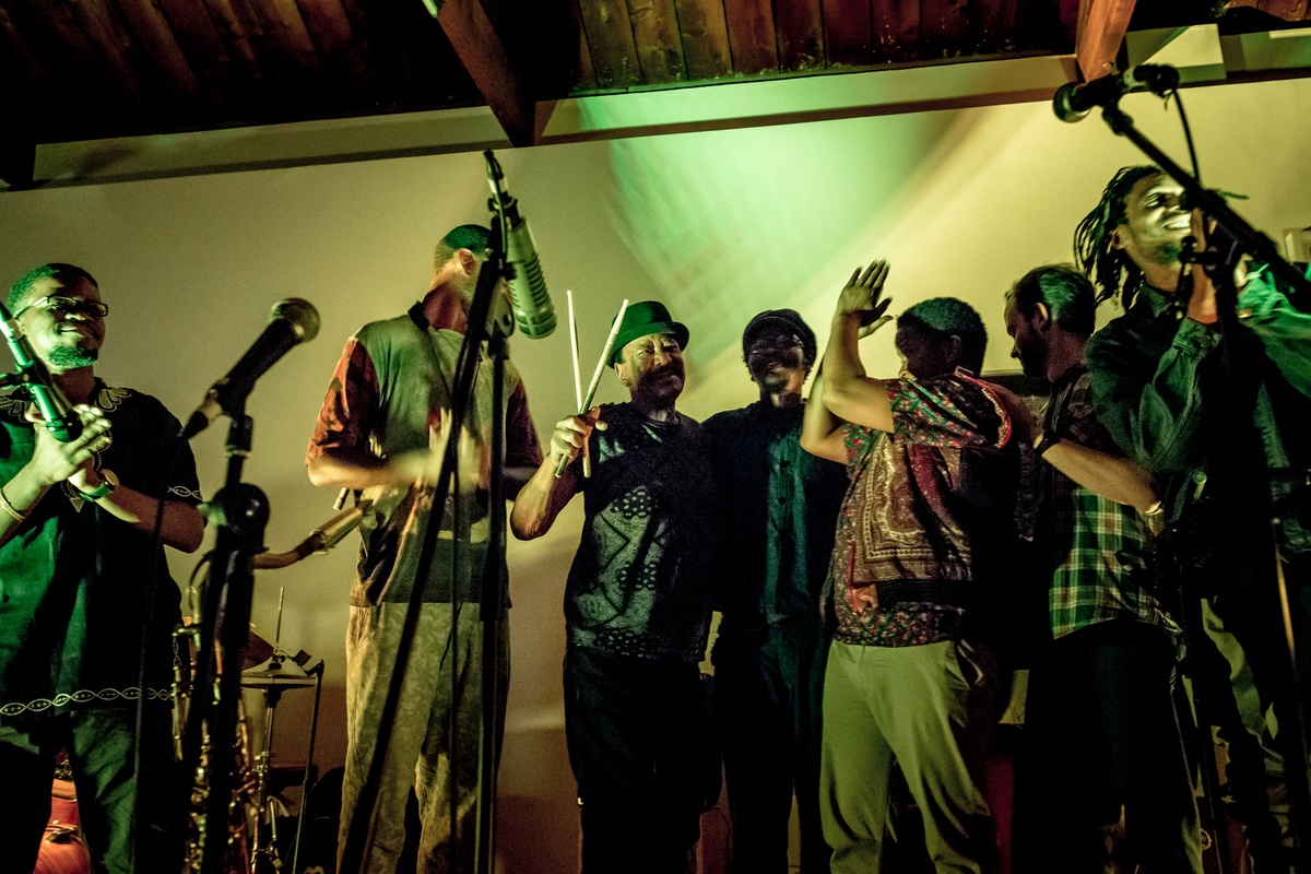 Event photograph from a performance by Shabaka and the Ancestors, with special guest Bra Louis Moholo-Moholo, on A4’s top floor that shows the musicians standing among microphone stands.
