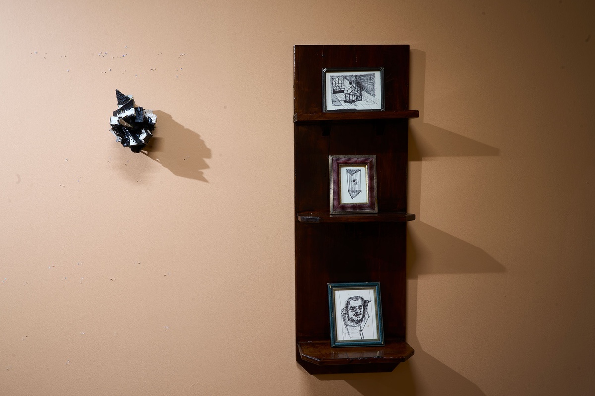 Installation photograph from Phillip Newman's exhibition in A4 Arts Foundation's Goods space. On the left, a sculptural object is mounted on the wall. On the right, three framed drawings are arranged on a three-tiered wooden shelf.
