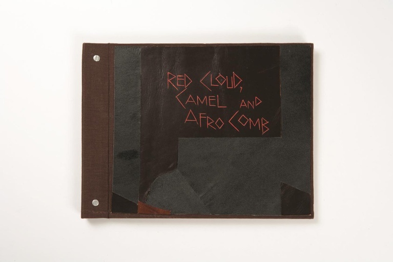 A top-down photograph of Peter Clarke's artist book 'Red Cloud, Camel and Afro Comb, Compiled in April 1997'.
