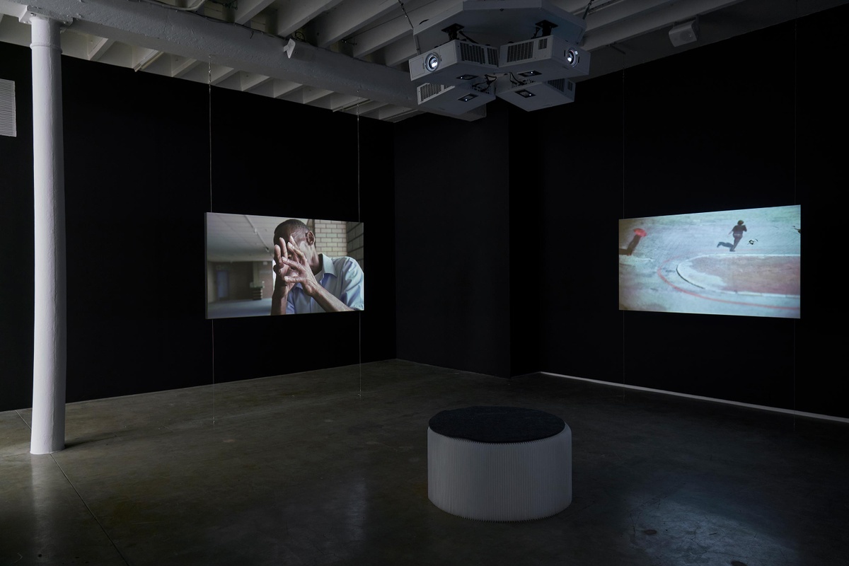 Installation photograph from the ‘Tell it to the Mountains’ exhibition in A4’s Gallery. On the left and right, two channels from Mikhael Subotzky’s video work ‘Moses and Griffiths’ is projected onto the walls in a darkened area of the gallery.
