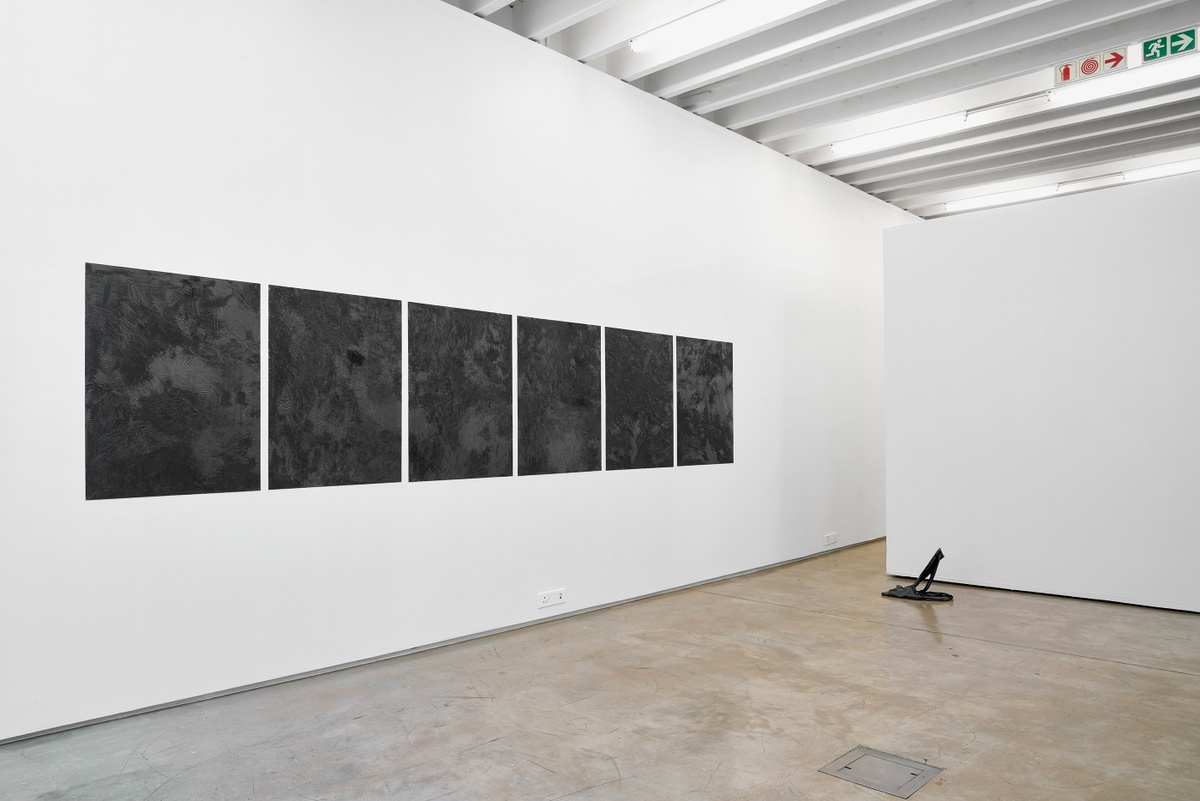 Installation photograph from the ‘without a clear discernible image’ exhibition in A4’s Gallery. On the left, six of Kevin Beasley’s graphite, ink and acrylic medium on paper works are mounted on the gallery wall. On the right, Beasley’s resin sculpture ‘Knees’ sits on the floor.
