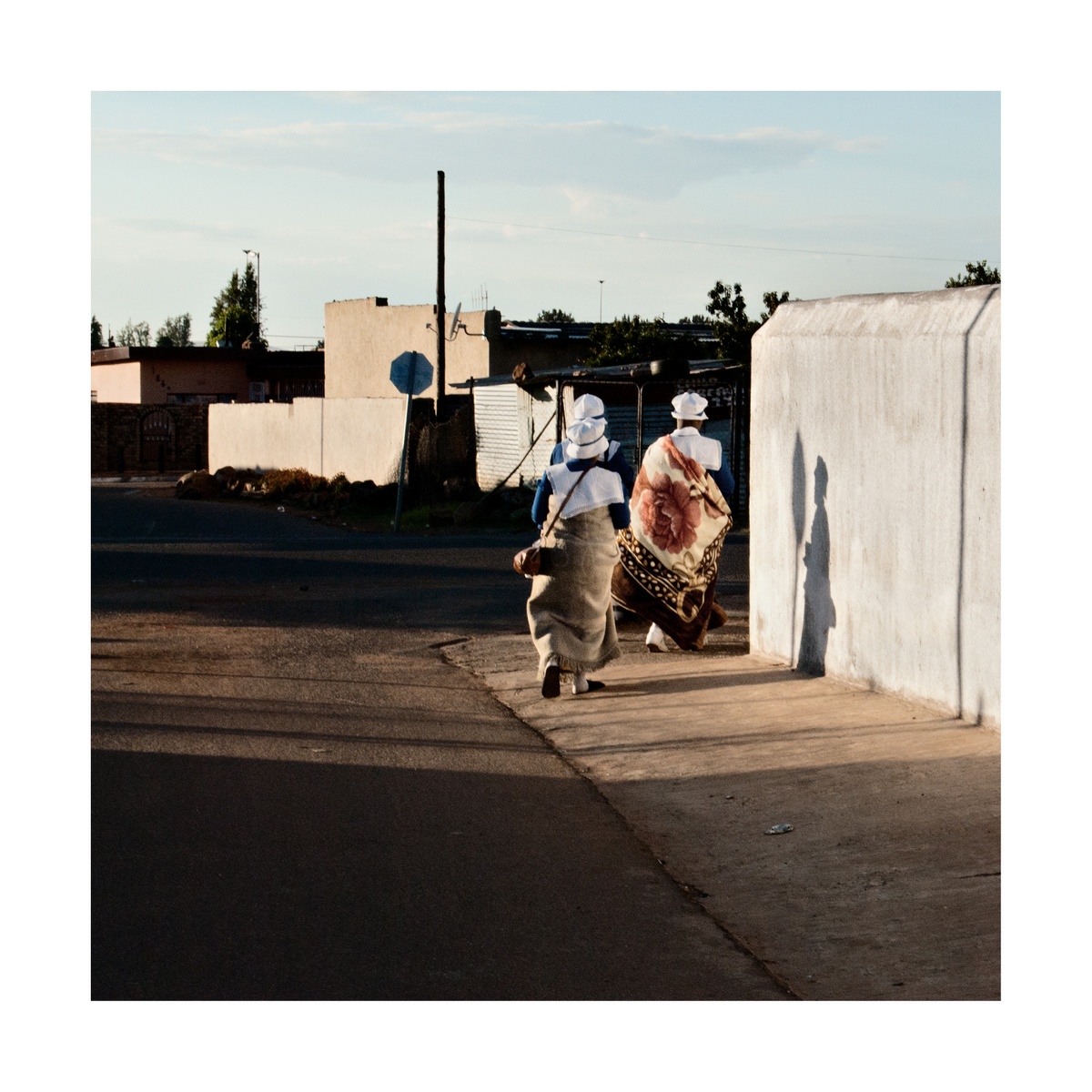 Photograph from Jabulani Dhlamini’s residency on A4’s top floor shows three individuals walking on a sidewalk wrapped in blankets.
