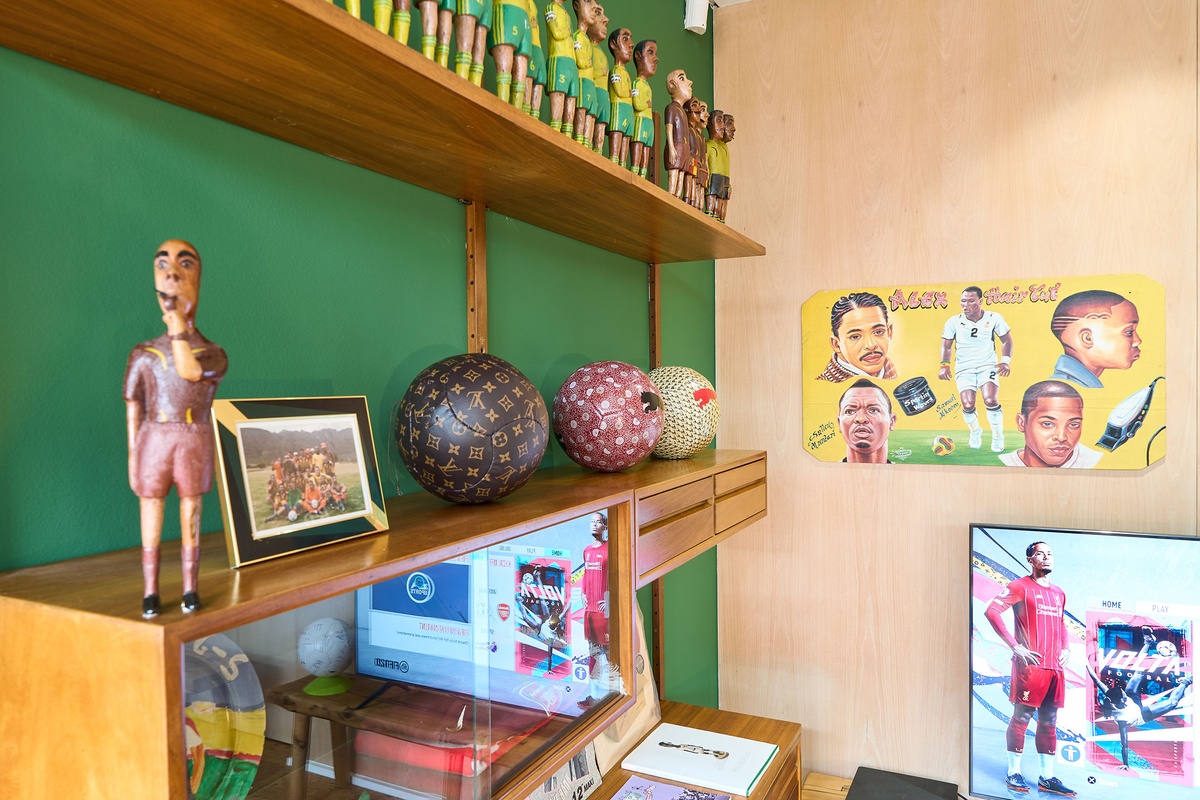 Installation photograph from the 2022 rendition of Exhibition Match on A4’s second floor. Closeup view of a wall-mounted wooden shelving unit that hosts Mikhael Subotzky’s photograph ‘Self-Portrait with Soccer Team, Voorberg Prison’ and Johannes Segogela’s ‘Bafana Bafana Soccer Team’ sculpture. 
