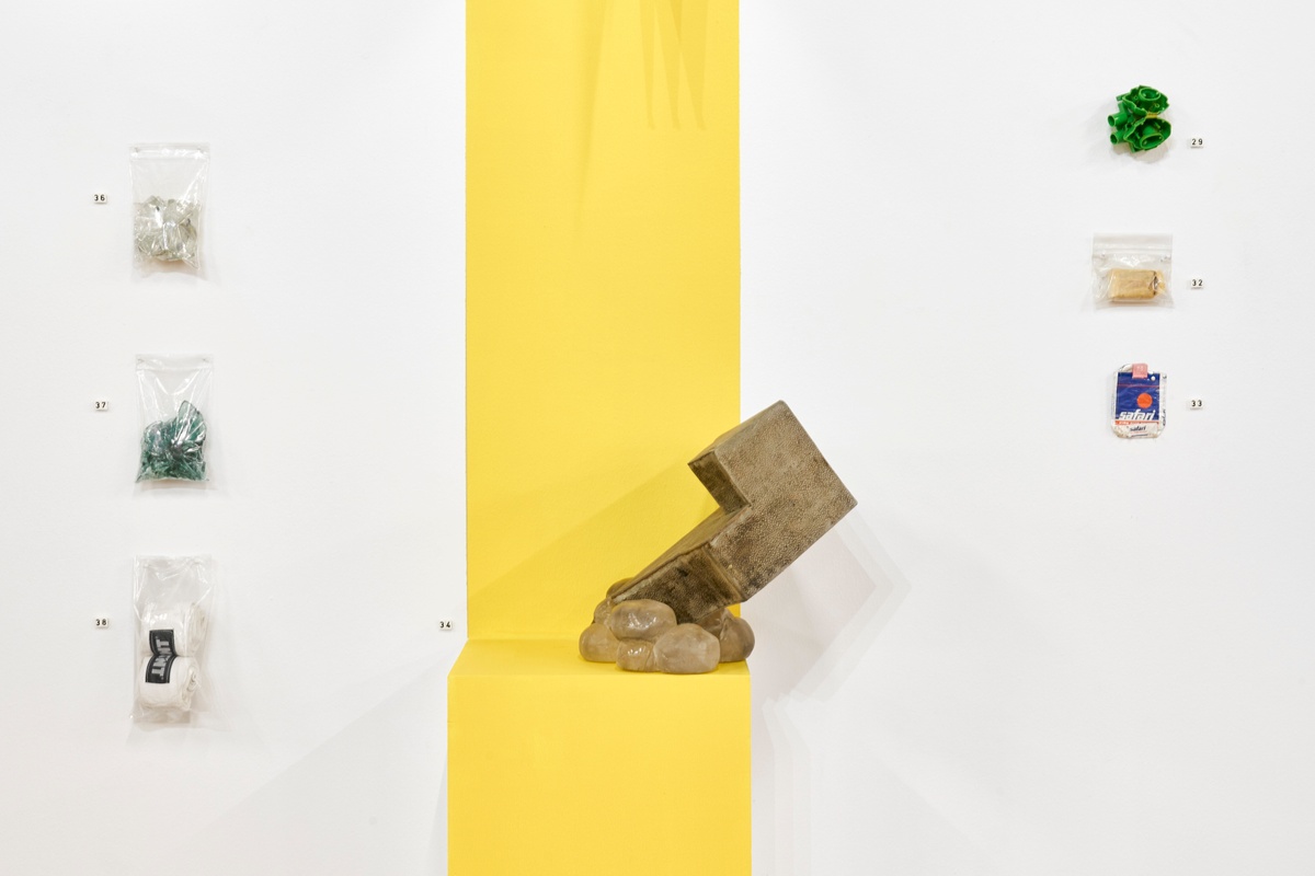 Installation photograph from ‘Archive as Terrarium: Part 3’ on A4’s top floor. In the middle, Christian Nerf and francis burger’s ‘And Not But’ sits on a plinth, with a column of yellow paint running across the plinth and the wall behind it.
