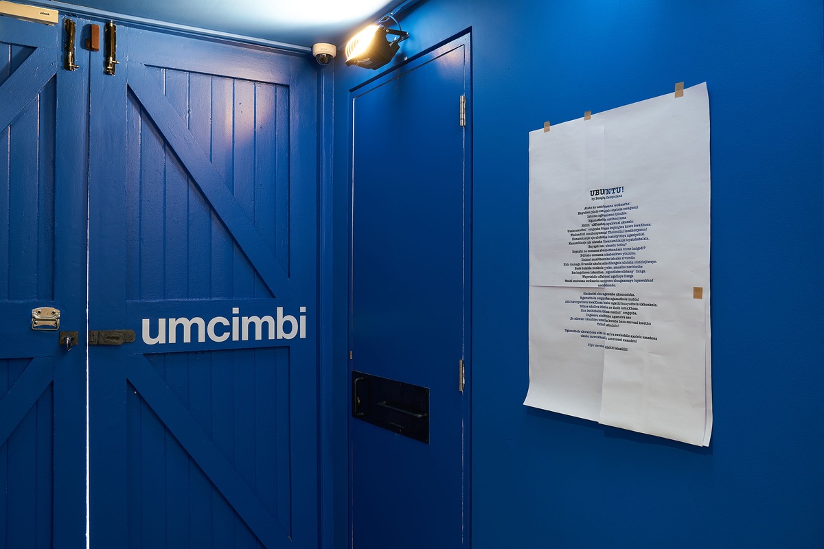 Installation photograph from the ‘Umcimbi’ exchange in A4’s Goods project space. On the right, the project title in white vinyl on the door. On the right, a print of Bonga Cempulana’s poem ‘Ubuntu!’.
