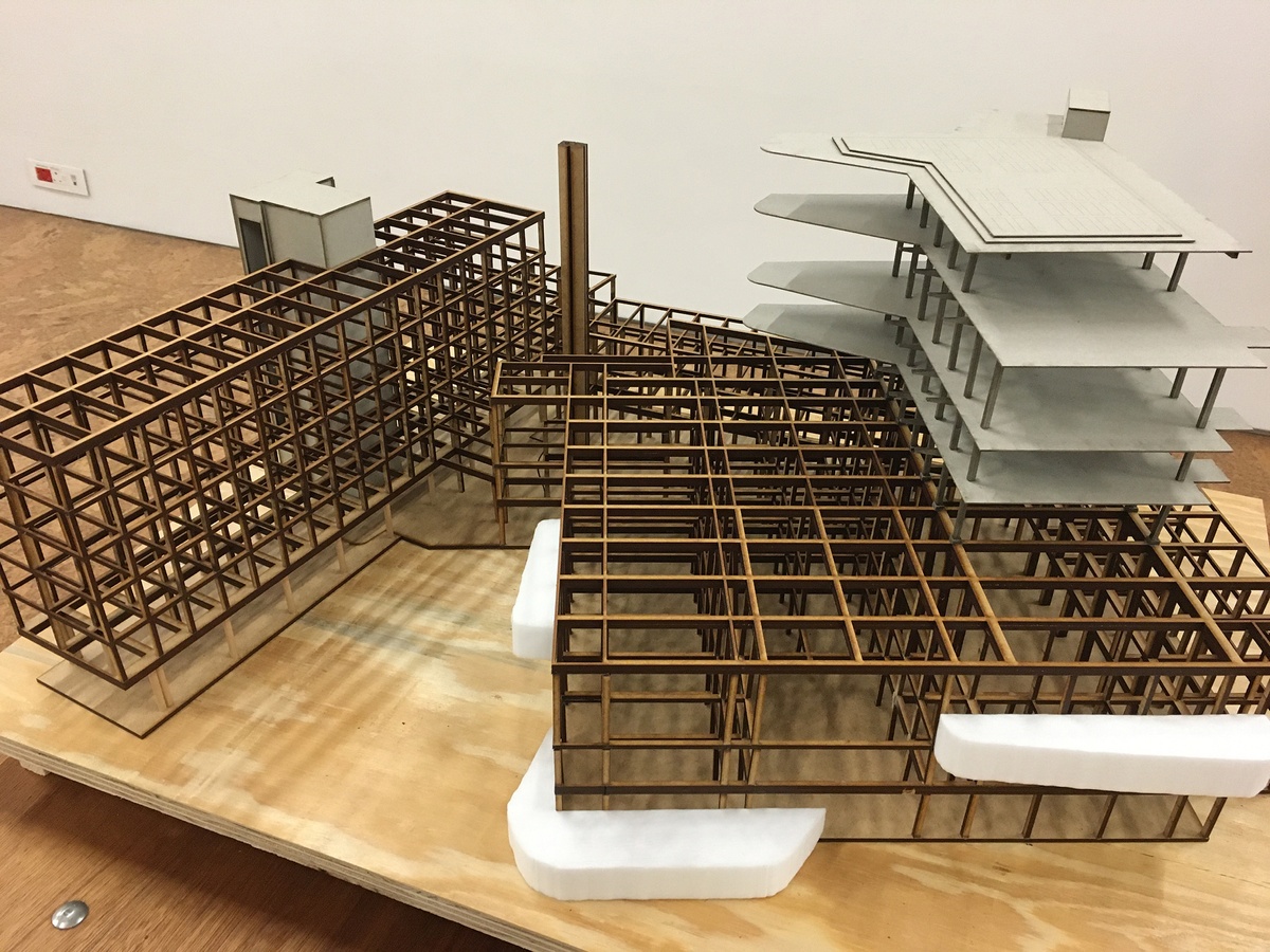 Photograph of an artwork from the Masters of Architecture Graduate Exhibition on A4’s top floor that depicts a wood and cardboard structural model of a building.
