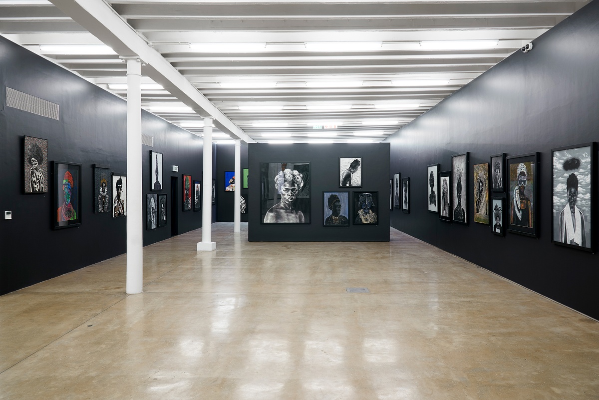 Installation photograph from the “Ikhono LaseNatali” exhibition in A4’s Gallery. In the middle, a black moveable gallery wall lined with various artworks. On the left and right, black gallery walls lined with various artworks.
