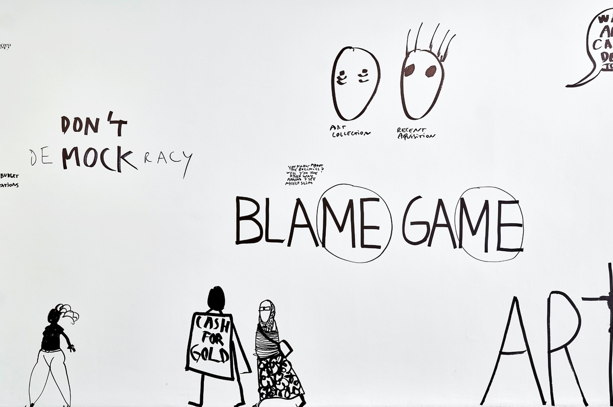 Installation photograph from Dan Perjovschi’s ‘The Black and White Cape Town Report’ exhibition in A4’s Gallery. A white gallery wall features black felt marker drawings with phrases like ‘Blame Game’, where the letters ‘ME’ are encircled, and two drawings of faces that illustrate ‘art collection’ (baggy eyes) and 'recent acquisition’ (hair raised). 
