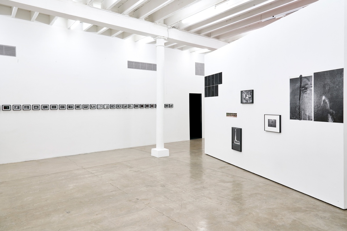 Installation photograph of the You to Me, Me to You exhibition. On the left, Bas Jan Ader’s 26 framed monochrome photographic prints ‘Study for In Search of the Miraculous (One Night in Los Angeles)’ are mounted on a white gallery wall in a straight line. On the right, Thembinkosi Hlatshwayo’s numerous photographic works are arranged on a white moveable gallery wall.
