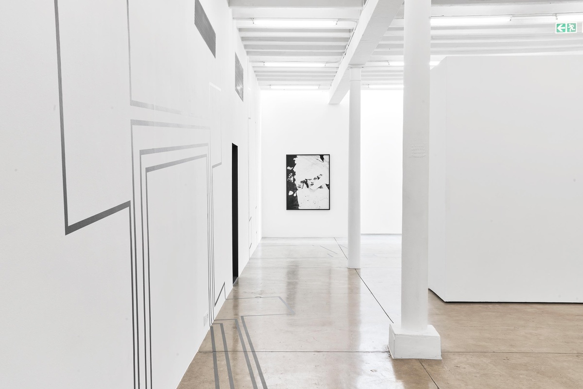 Installation photograph from the Customs exhibition in A4’s Gallery. On the left, a detail of Dor Guez’s vinyl wall installation ‘Double Stitch’ on a white gallery wall. In the back, Dor Guez’s photographic print ‘Samira’ is mounted on a white gallery wall.
