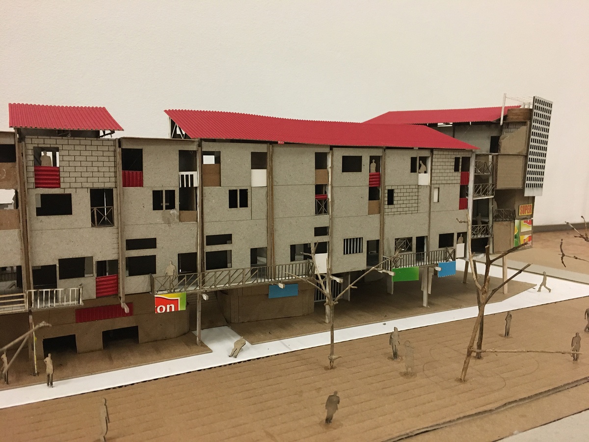 Photograph of an artwork from the Masters of Architecture Graduate Exhibition on A4’s top floor. A cardboard model of a building with a ground floor that’s smaller than it’s other floors.
