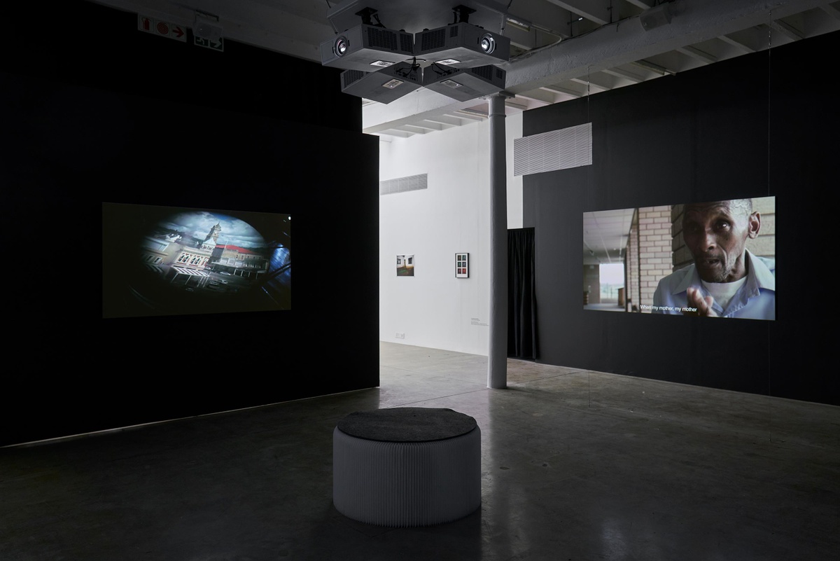 Installation photograph from the ‘Tell it to the Mountains’ exhibition in A4’s Gallery. On the left and right, two channels from Mikhael Subotzky’s video work ‘Moses and Griffiths’ is projected onto the walls in a darkened area of the gallery.
