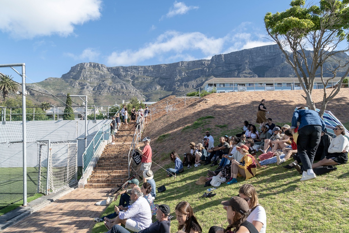 Match day photograph from the 2022 rendition of Exhibition Match that shows viewers seated on a mound covered in grass.
