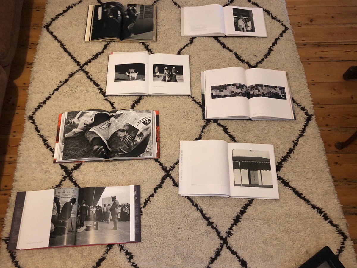 Process photograph from the ‘Picture Theory’ exhibition in A4’s Gallery. A topdown view shows a selection of David Goldblatt’s photo-books laid out on a carpet on a wooden floor.
