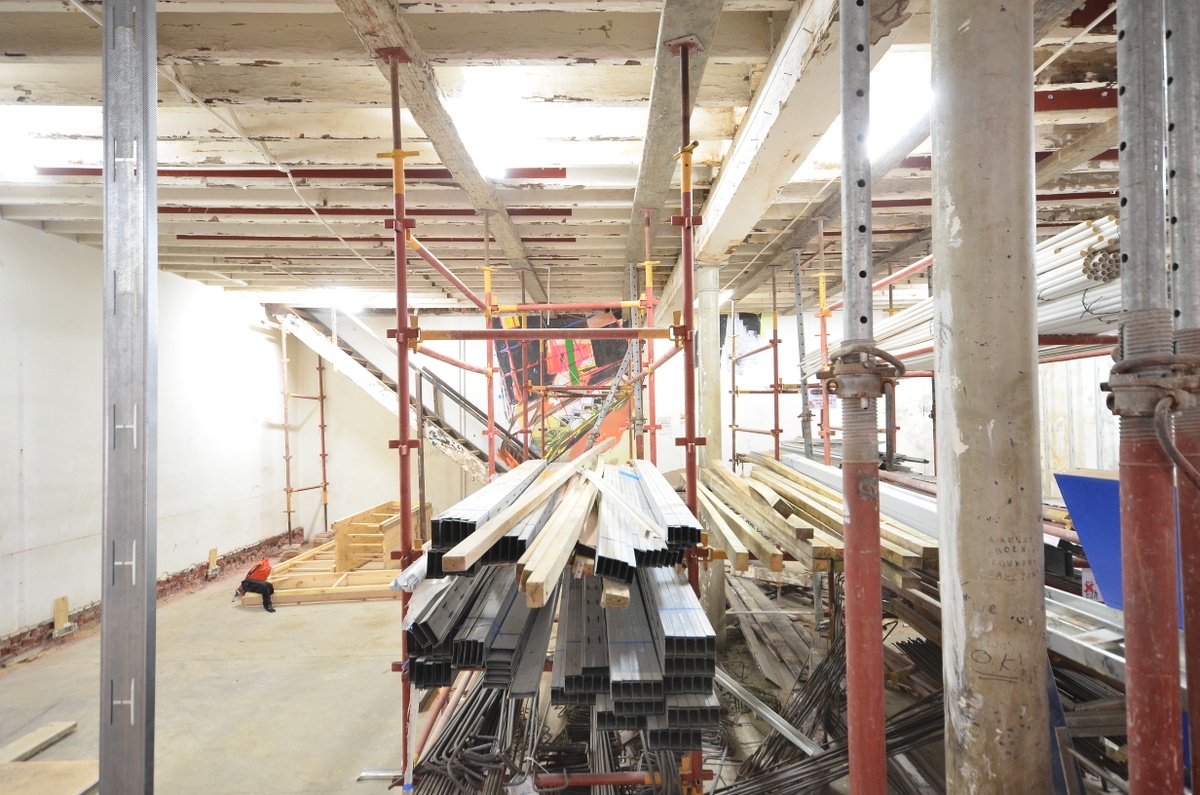 Process photograph from Dorothee Kreutzfeldt’s residency on A4’s 1st floor. At the front, metal scaffolding holds metal and wood support beams. At the back, a painted mural on the wall adjacent to the staircase.
