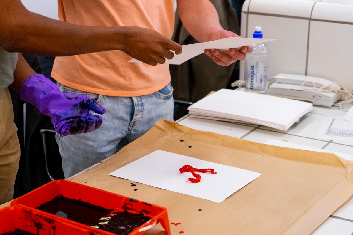 Event photograph from ‘Knots’, a conversation between Igshaan Adams and Josh Ginsburg, marking the close of ‘Open Production’, Adams’ hybrid studio/exhibition in A4’s Gallery. At the reception desk, A4 staff members facilitate an interactive exchange where attendees can create artworks by using threads dipped in dye as a drawing medium.
