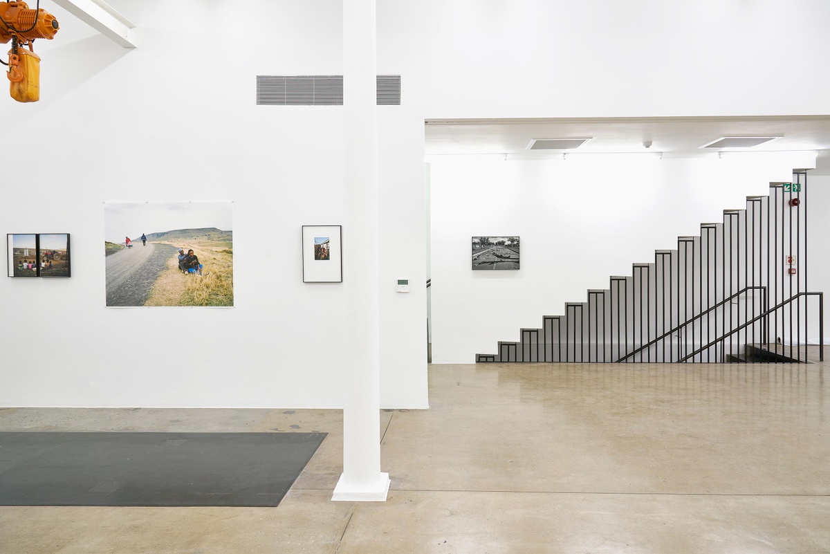 Installation photograph from the ‘Tell it to the Mountains’ exhibition in A4’s Gallery. On the left, Lindokuhle Sobekwa’s photographs ‘Kwa MamThembu’, ‘Estopin Qumbu’ and ‘Yonelisa Samela in his grandmother’s garden during South Africa’s first lockdown’ are mounted on the wall. On the right, Sobekwa’s monochrome photograph ‘After a protest related to continuous power cuts during Lockdown Level 5 in Thokoza’ is mounted on the wall above the stairway.
