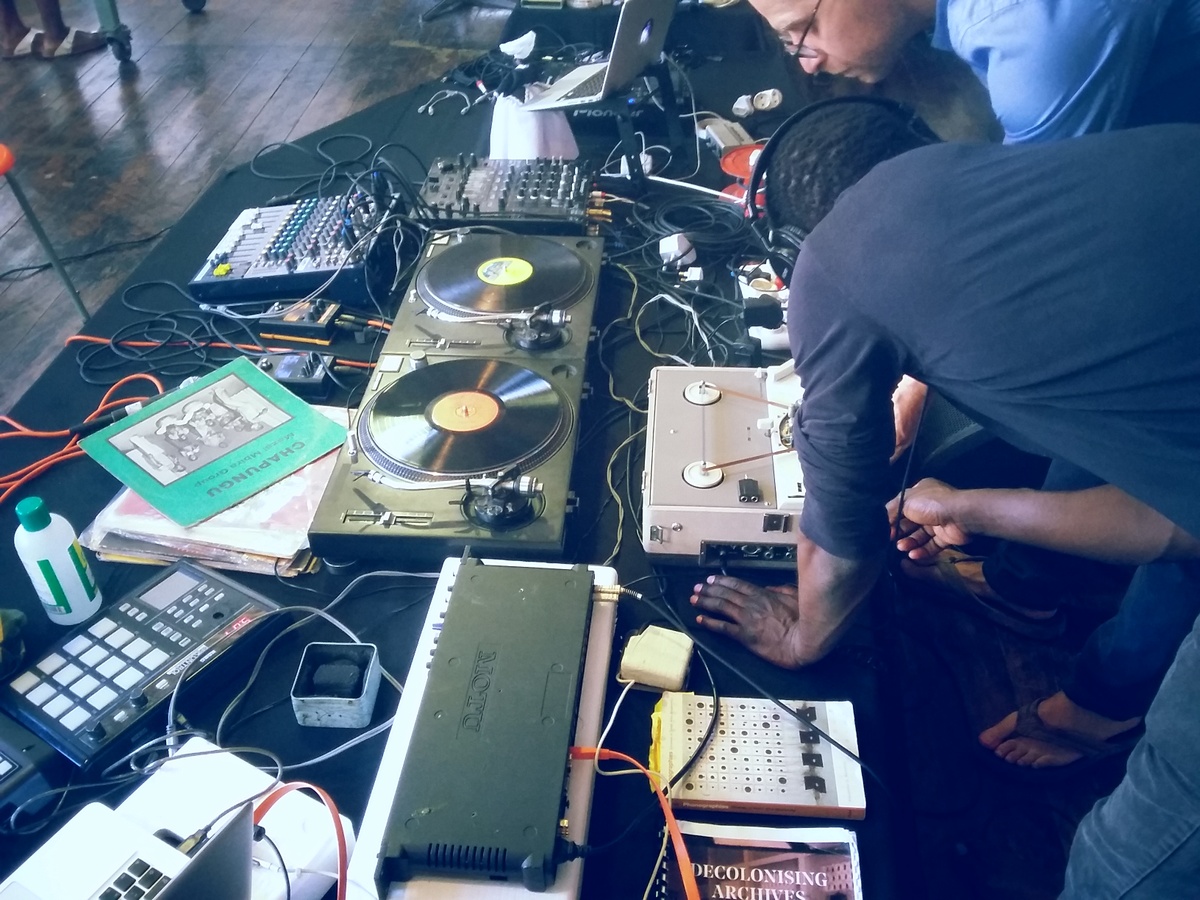 Event photograph from the offsite exchange ‘Pungwe Nights: Listening to Listening’ that shows a table laden with audio equipment, laptops and vinyl records.

