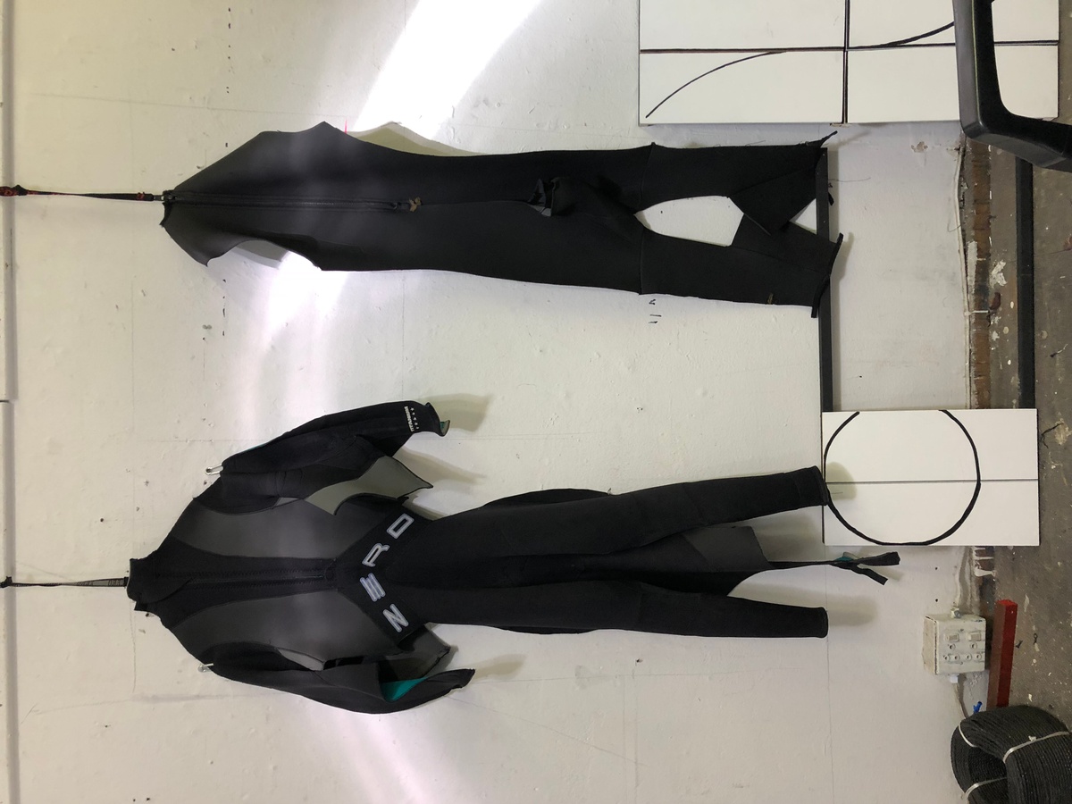 Process photograph from Unathi Mkonto’s interactive installation ‘AVOID’ on A4’s ground floor that shows two partially deconstructed wetsuits hanging on a white wall.
