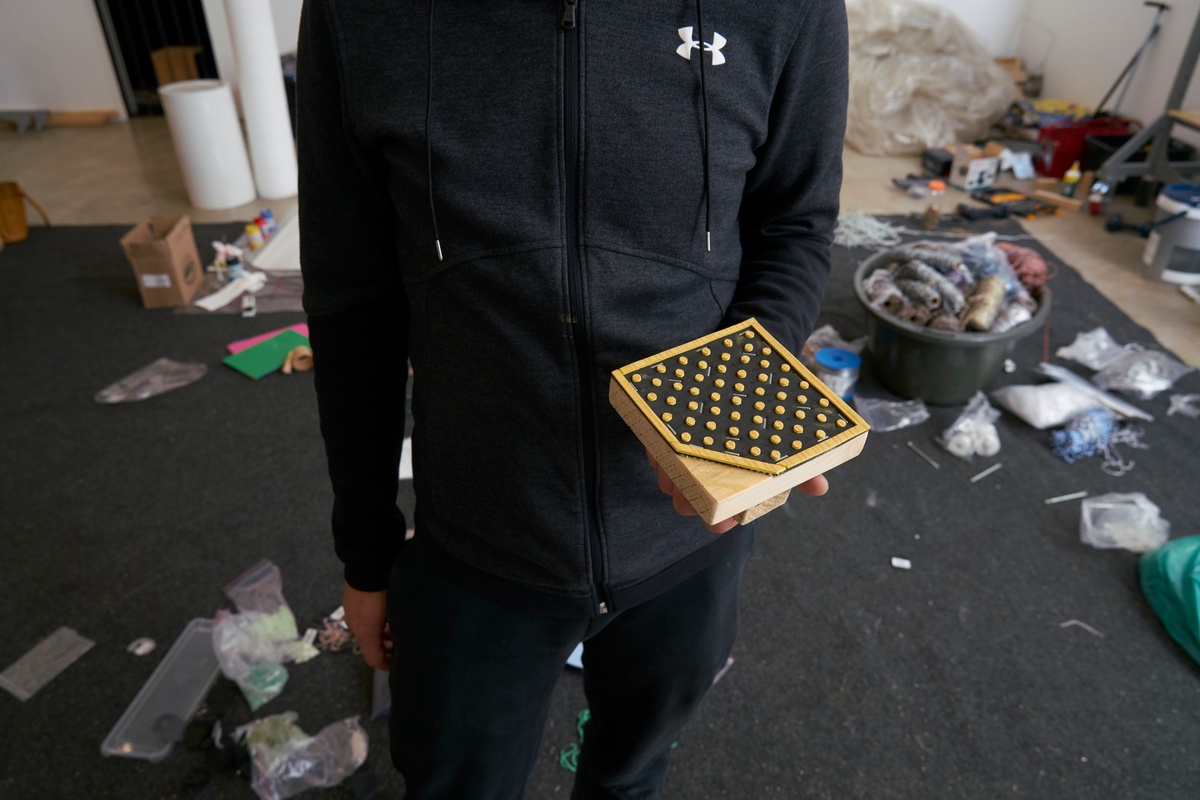 Process photograph from ‘Open Production’, Igshaan Adams’ hybrid studio/exhibition in A4’s Gallery. An individual holds a printing block with a patterned design used to apply dyes to woven fabrics or tapestries.
