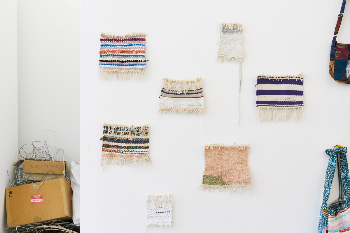 Event photograph from the Scalabrini Workshop that formed part of ‘Open Production’, Igshaan Adams’ hybrid studio/exhibition in A4’s Gallery. Swatches of woven fabric bordered with loose threads arranged on a white wall.
