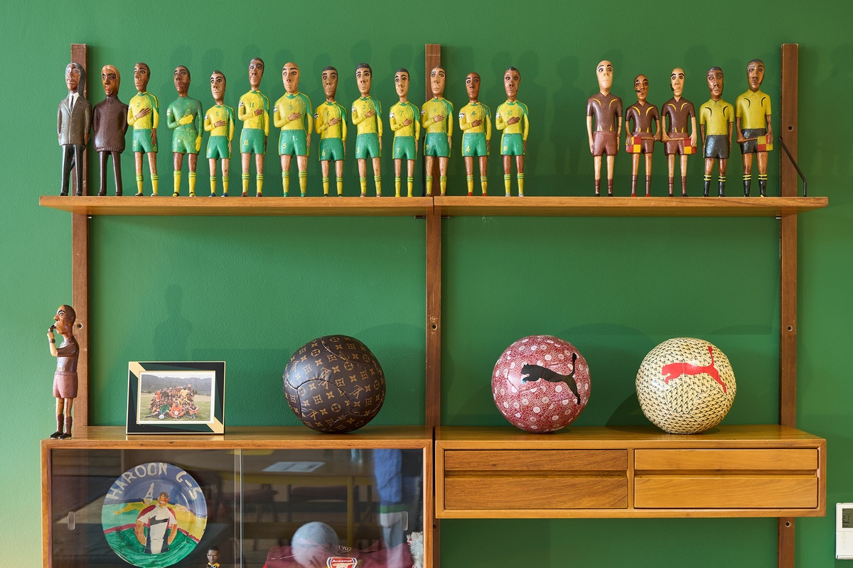 Installation photograph from the 2022 rendition of Exhibition Match on A4’s second floor. Closeup view of a wall-mounted wooden shelving unit that hosts Mikhael Subotzky’s photograph ‘Self-Portrait with Soccer Team, Voorberg Prison’ and Johannes Segogela’s ‘Bafana Bafana Soccer Team’ sculpture. 
