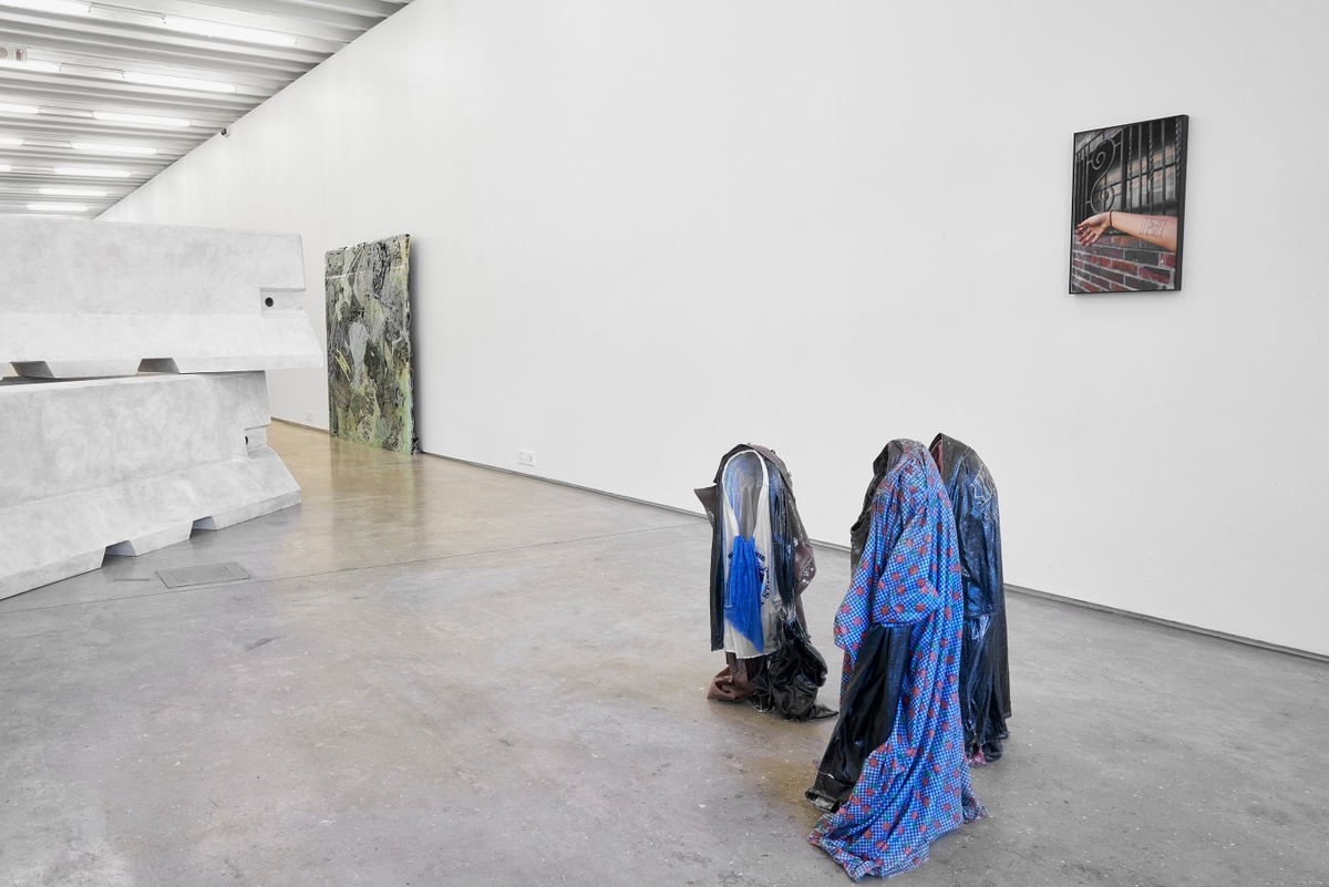 Installation photograph from the ‘without a clear discernible image’ exhibition in A4’s Gallery. At the front, Kevin Beasley’s garment and resin sculptures ‘Untitled (Brooklyn kid)’, ‘Untitled (kid I)’ and ‘Untitled (kid II)’ stands on the floor in a huddle. On the right, Beasley’s photograph ‘Windows’ is mounted on the gallery wall. On the left, Beasley’s untitled plywood and paint sculpture sits on the gallery floor.
