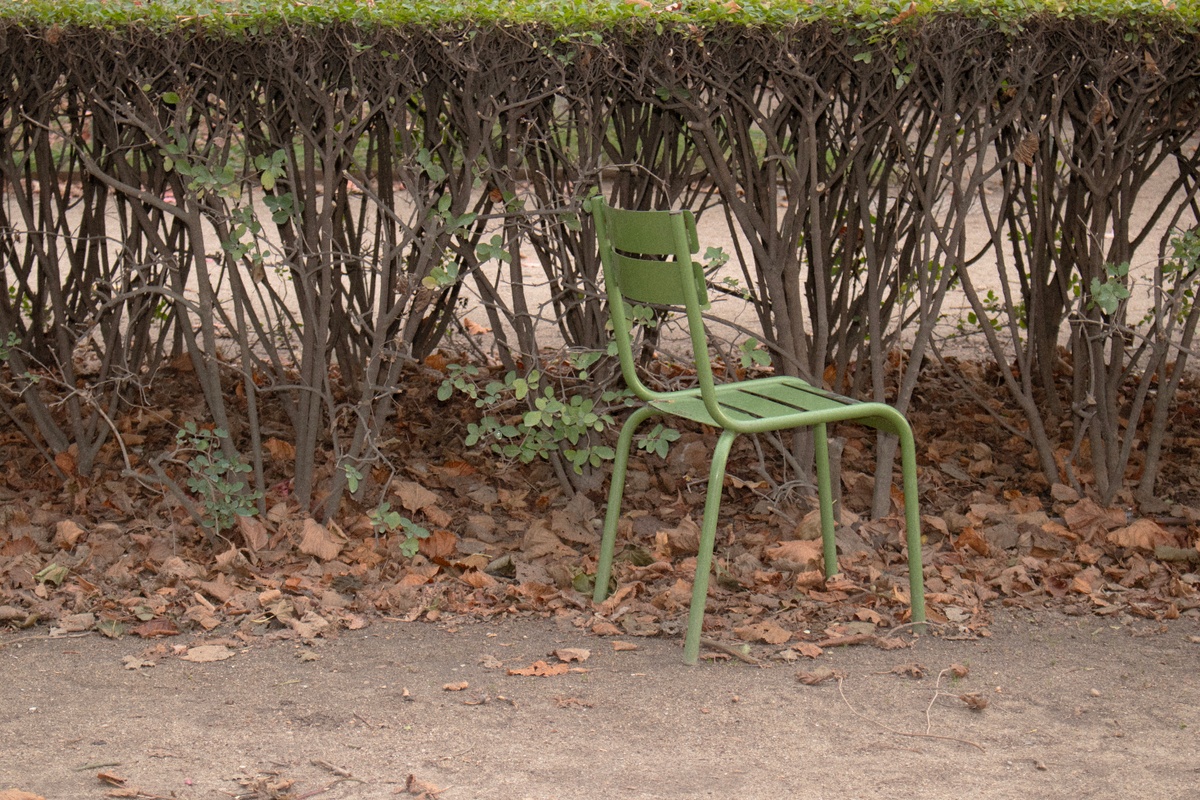 A photographic print from Thembinkosi Hlatshwayo’s ‘hearts can’t make it up’ series that depicts one green chair arranged in front of a hedge.
