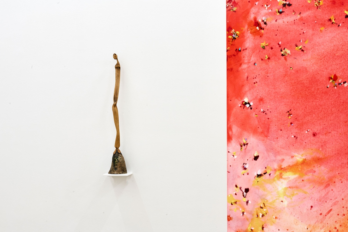 Installation photograph from the 'A Little After This' exhibition in A4 Arts Foundation's gallery. On the left, Lucas Sithole's carved yellowwood sculpture 'Not You!' sitting on a small wall-mounted shelf. On the right, an installation of Penny Siopis' glue, ink and oil 'Maitland' paintings suspended from the ceiling.
