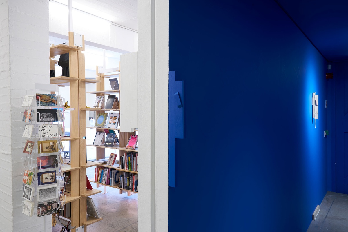 Installation photograph from Guy Simpson's Passage exhibition in A4 Arts Foundation's Goods space shows two sculptures that recall the mezuzah attached to the wall. At the front, one wood sculpture is painted blue to match the wall. At the back, another wood and electrical wire sculpture is unpainted.
