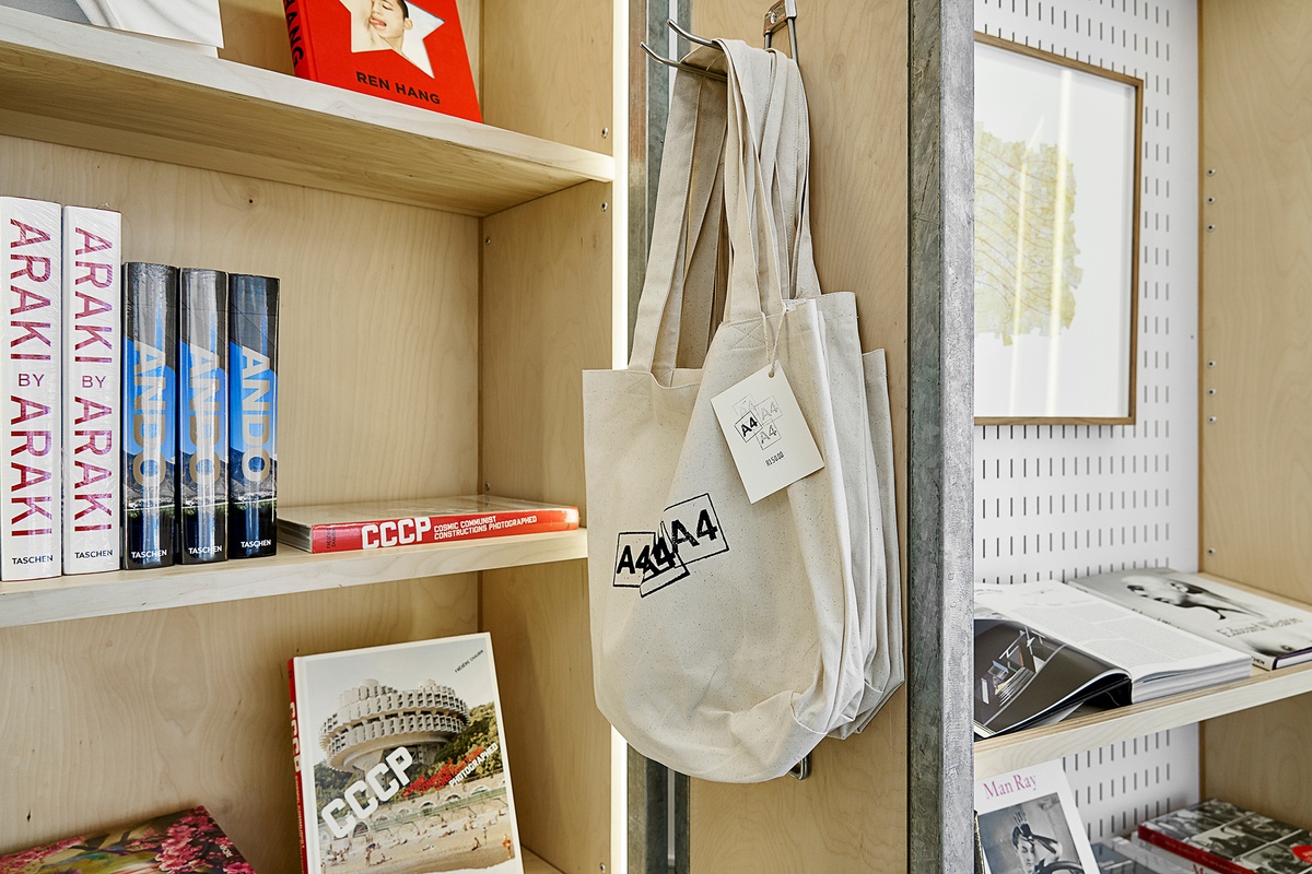 Installation photograph from the Taschen pop-up in A4’s Proto~ museum shop. In the middle, a close-up view of a cabinet shelf shows A4 tote bags hanging on a metal hook. 
