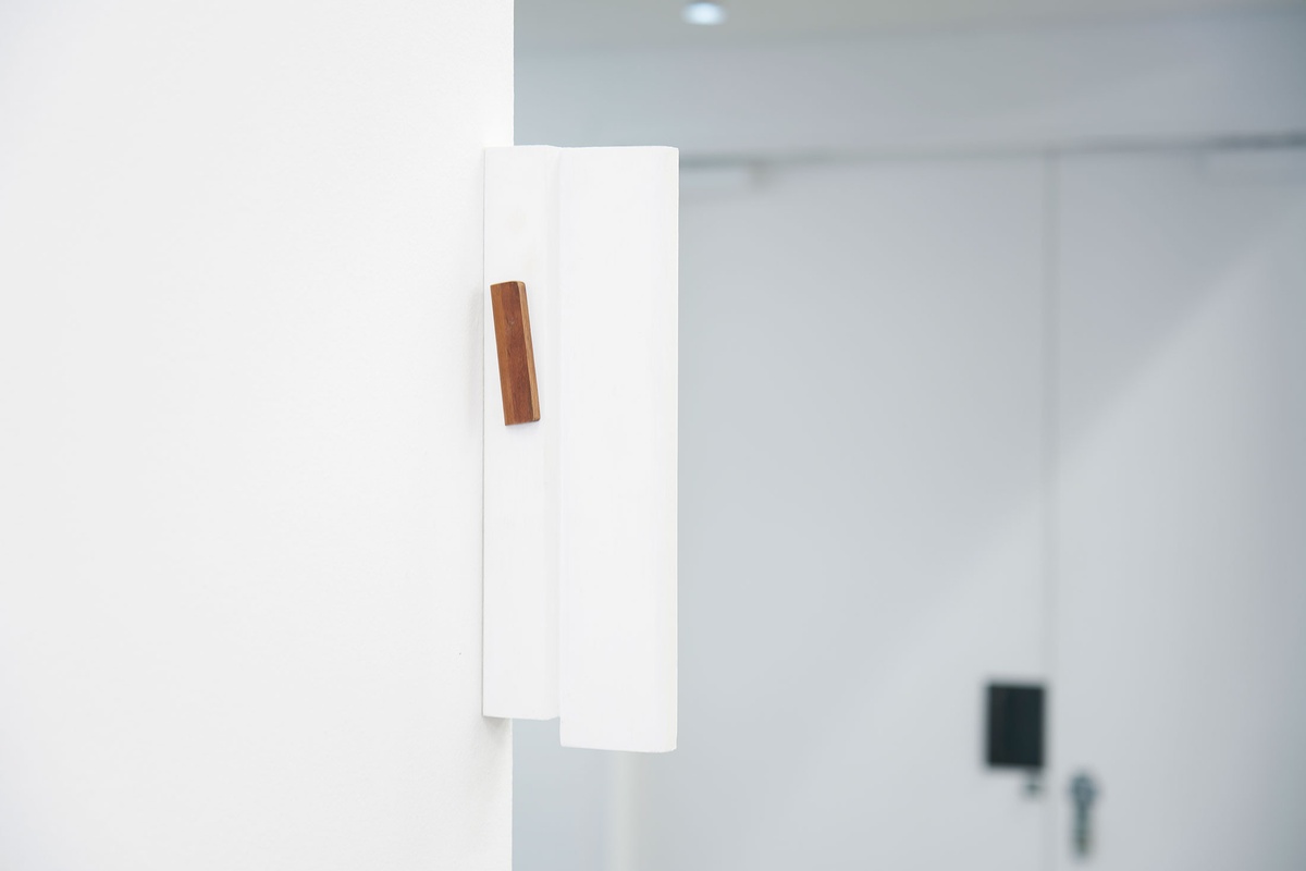 Installation photograph from Guy Simpson's Passage exhibition in A4 Arts Foundation's Goods space shows a partially white-painted wooden sculpture that recalls the mezuzah attached to the edge of the white wall.
