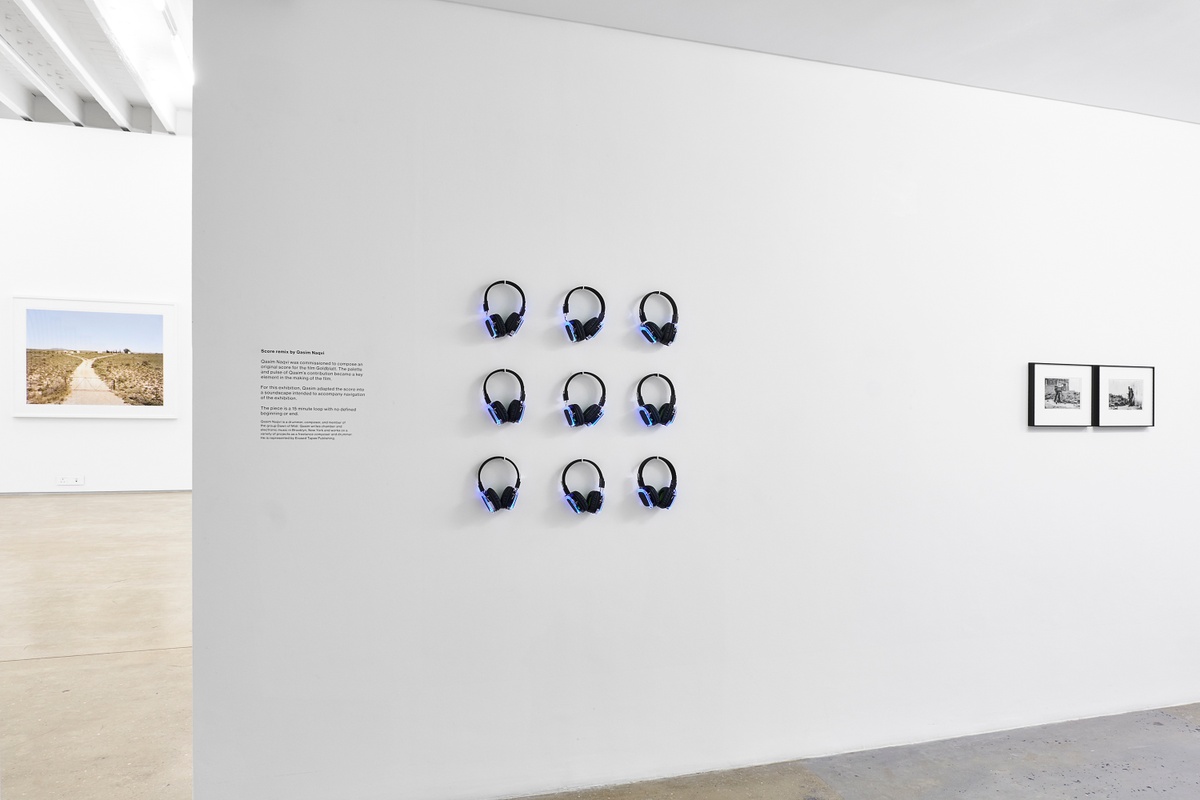 Installation photograph from the ‘Picture Theory’ exhibition in A4’s Gallery. On the left, Qasim Naqvi’s audio installation ‘Score remix’ consists of a grid of wall-mounted headphones. On the right, David Goldblatt’s homonymous monochrome photographs ‘Photographer and client, Braamfontein. Johannesburg,1955’ are mounted on the gallery wall.
