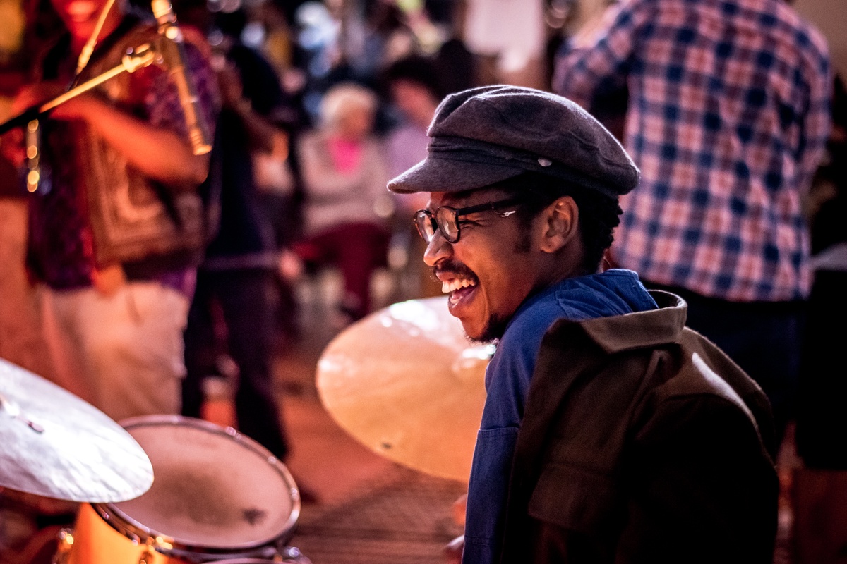 Event photograph from a performance by Shabaka and the Ancestors, with special guest Bra Louis Moholo-Moholo, on A4’s top floor that shows a musician seated at a drum set.
