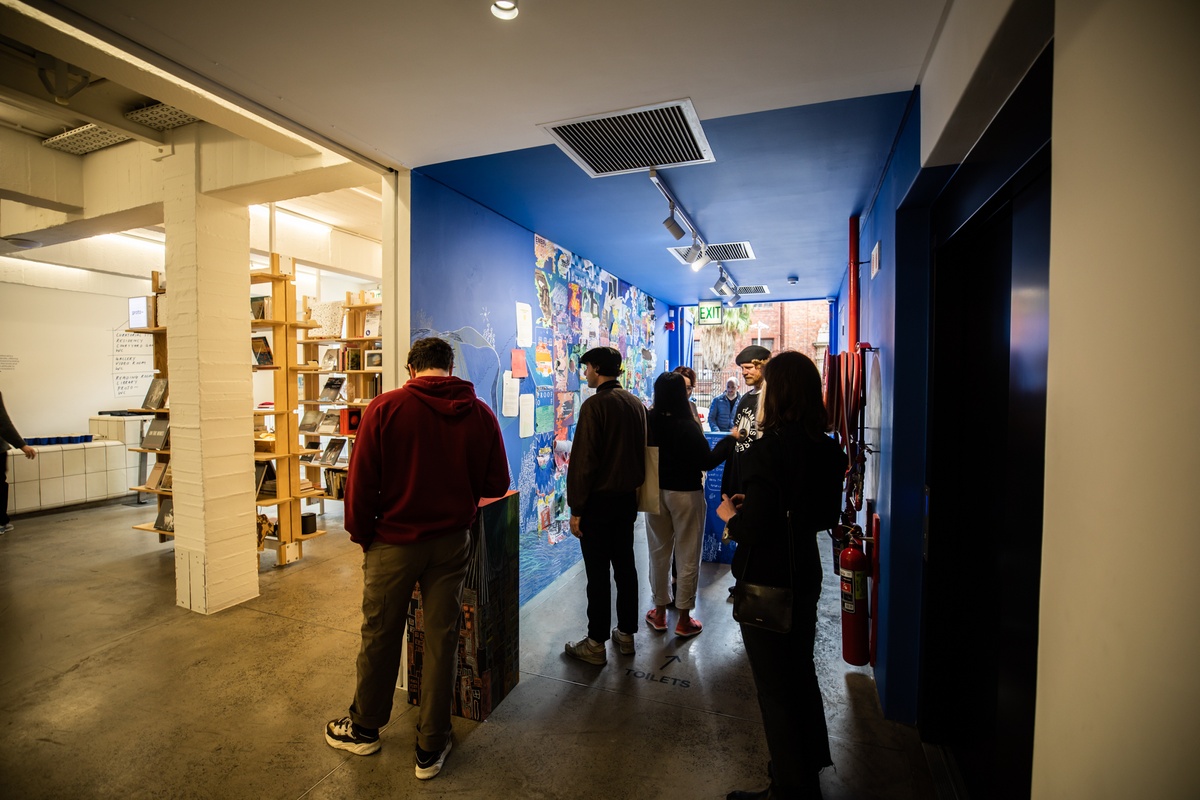 Event photograph from the opening of ‘Disruption’, Hanna Noor Mahomed’s residency in A4’s Goods project space, shows attendees standing around the exhibition space.
