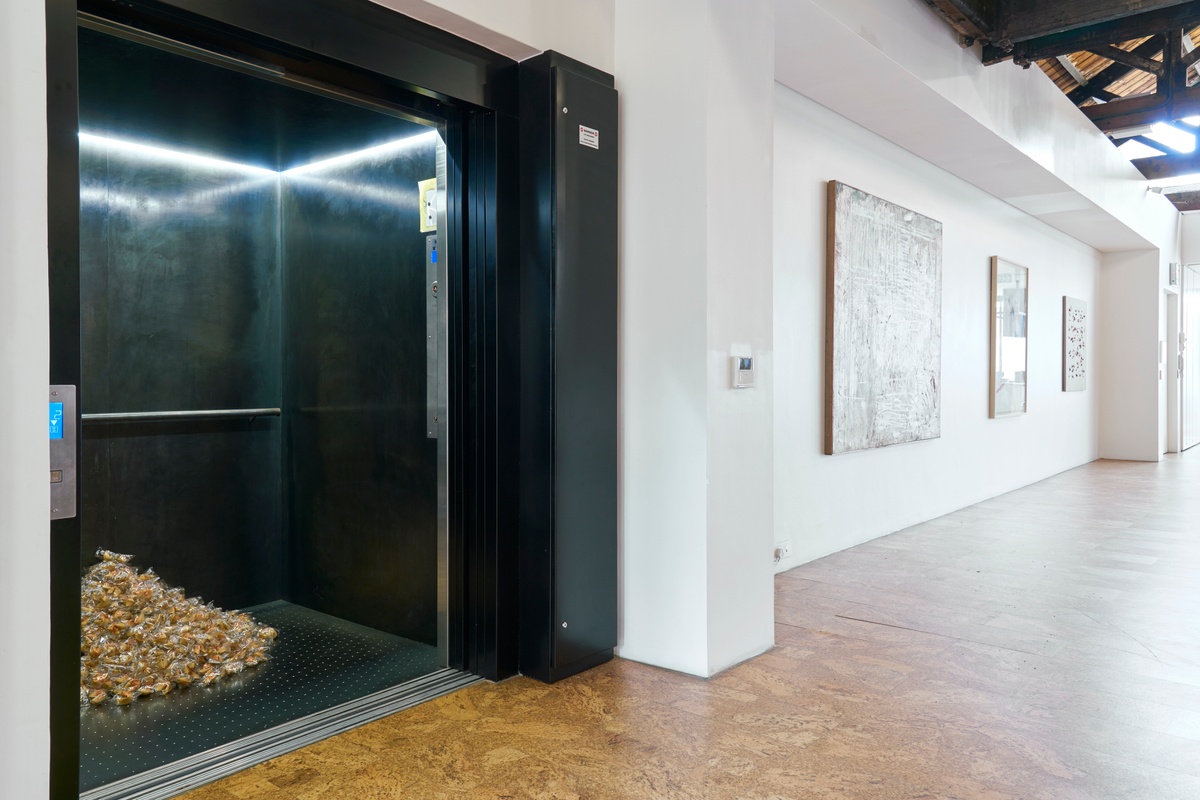 Installation photograph of Felix González-Torres' ‘Untitled (Fortune Cookie Corner)’ in A4’s elevator, with wrapped fortune cookies piled against the back of the interior.
