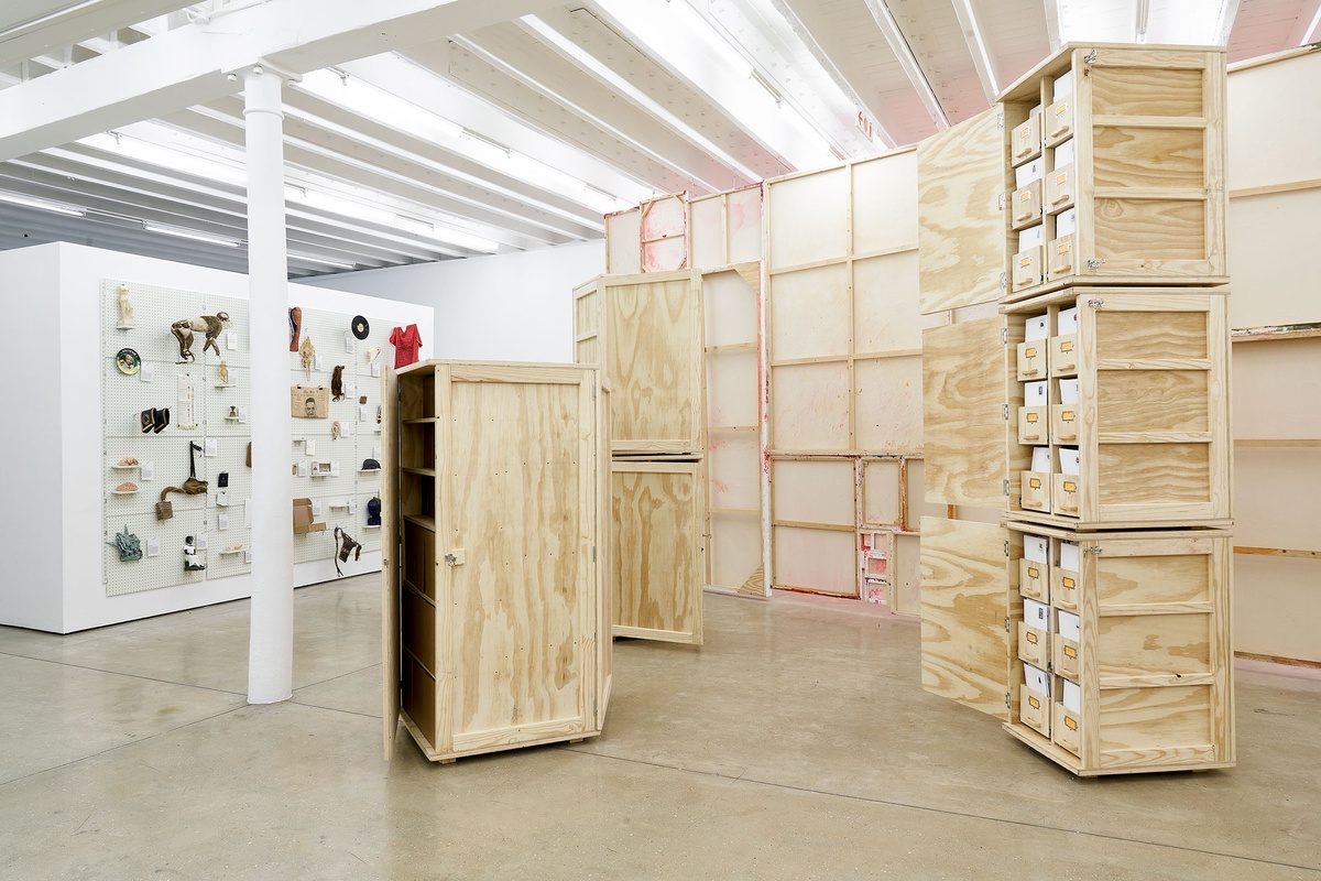 Installation photograph from the 'A Little After This' exhibition in A4 Arts Foundation's gallery. On the right, collected objects from Penny Siopis' 'Will' work are stored in envelopes and wooden crates. On the left, collected objects from Penny Siopis' 'Will' work mounted on a white moveable gallery wall through the use of perforated metal panels.
