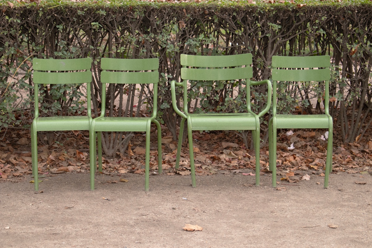 A photographic print from Thembinkosi Hlatshwayo’s ‘hearts can’t make it up’ series that depicts four green chairs arranged in front of a hedge.
