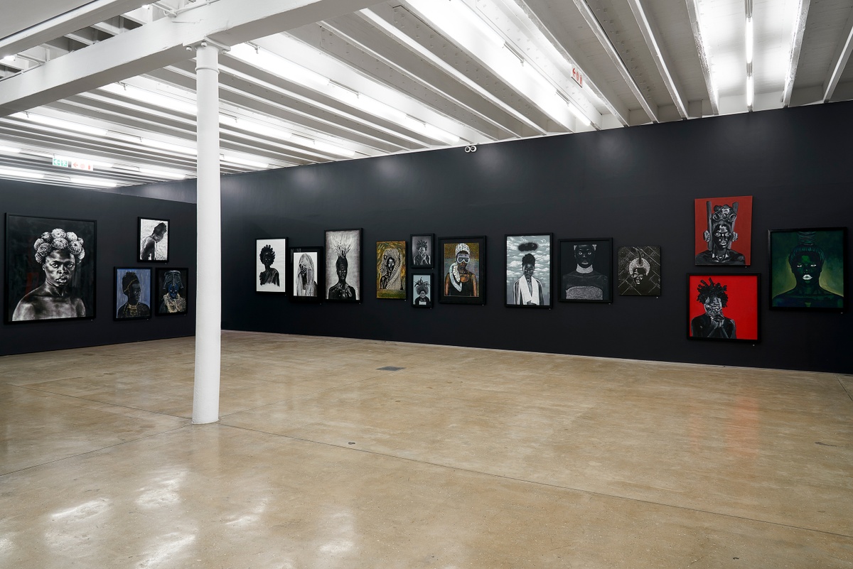 Installation photograph from the “Ikhono LaseNatali” exhibition in A4’s Gallery. On the left, various artworks are mounted on a black moveable gallery wall. On the right, various artworks line the black gallery wall.
