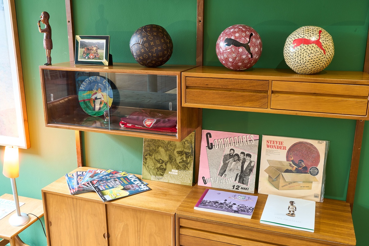 Installation photograph from the 2022 rendition of Exhibition Match on A4’s second floor. Closeup view of a wall-mounted wooden shelving unit that hosts Mikhael Subotzky’s photograph ‘Self-Portrait with Soccer Team, Voorberg Prison’ and Johannes Segogela’s ‘Bafana Bafana Soccer Team’ sculpture. 
