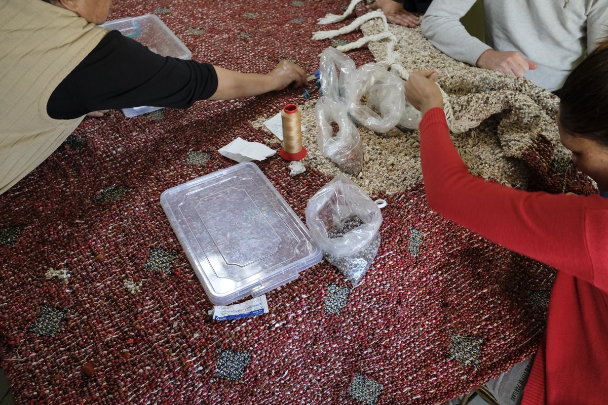 Process photograph from a visit to the Bonteheuwel township that formed part of ‘Open Production’, Igshaan Adams’ hybrid studio/exhibition in A4’s Gallery. A closeup view of various people working on one of Adams’ mixed media tapestries.
