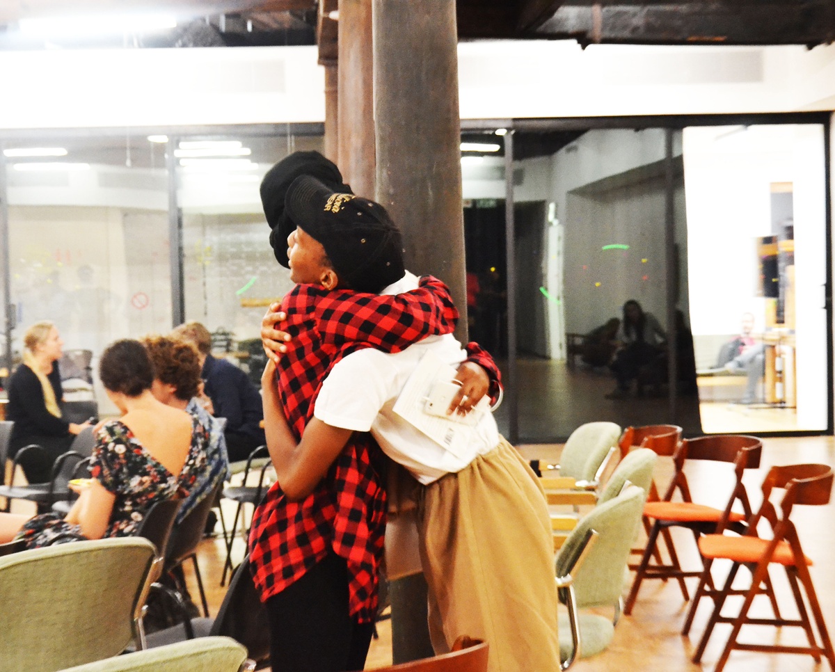 Event photograph from book launch of ‘The Truth Shall Bloom’ by Tabogo Nong on A4’s top floor that shows two attendees embracing in front of a support beam.

