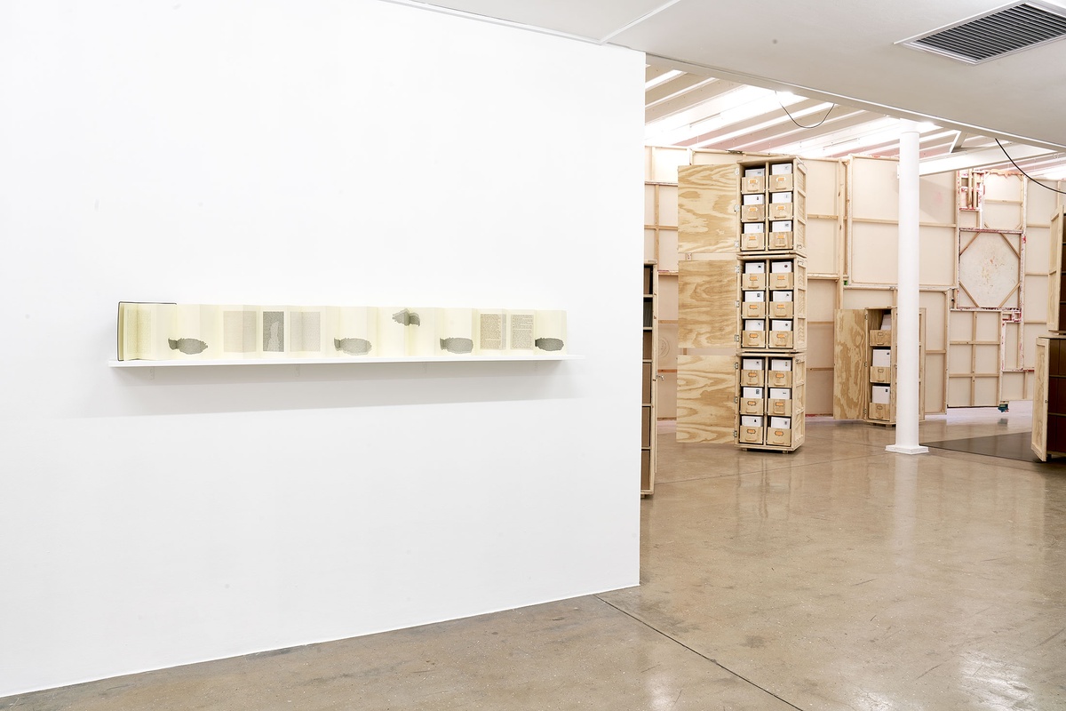 Installation photograph from the 'A Little After This' exhibition in A4 Arts Foundation's gallery. On the left, Colin Richards' Moleskin, collage and ink work 'A Little After This' displayed on a wall-mounted shelf. On the right, collected objects from Penny Siopis' 'Will' work are stored in envelopes and wooden crates.
