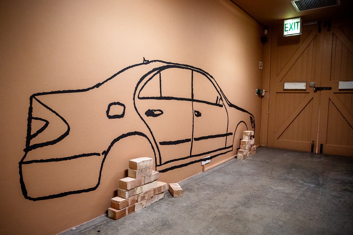 Event photograph from the preview of the 'A Little After This' exhibition in A4 Arts Foundation. On the left, Robin Rhode's stencil and brick artwork 'Car on Bricks (Sedan/Mercedes)' installed in the Goods space.
