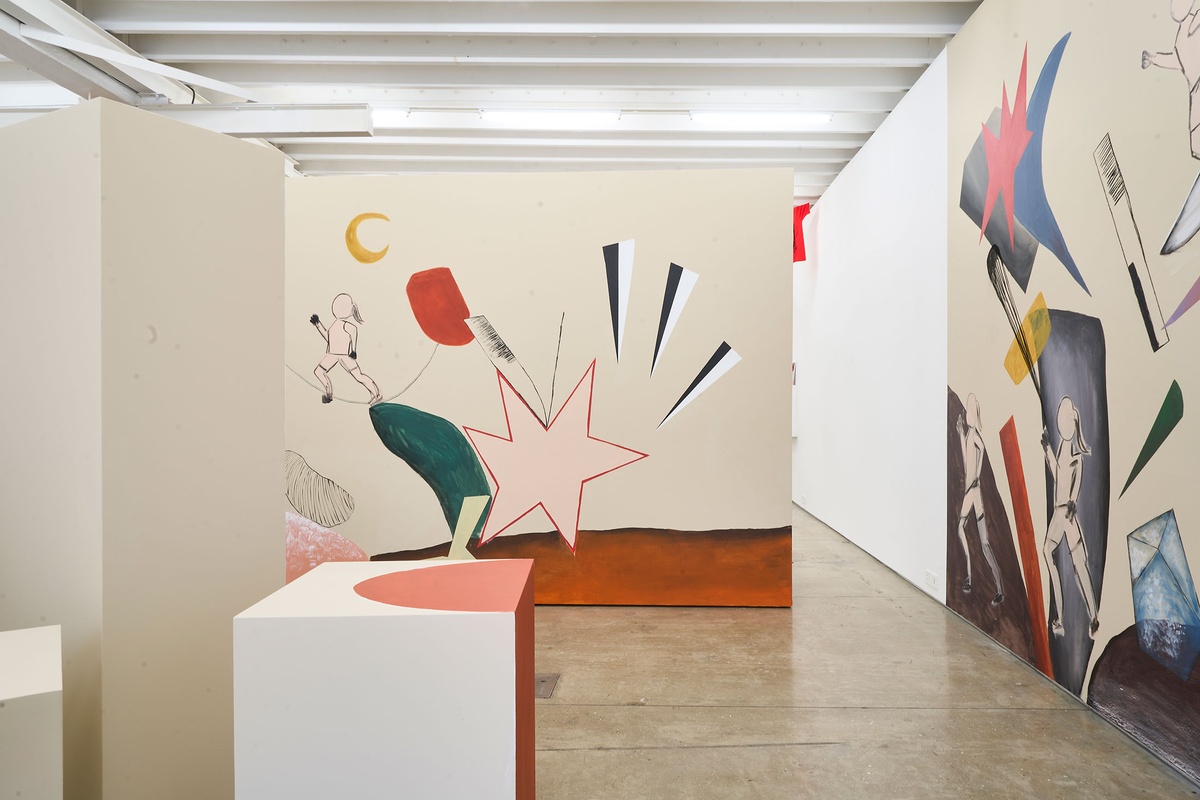 Installation photograph of Common exhibition, featuring an installation by Hanna Noor Mahomed called ‘The Prodigal Daughter.’ On the right and at the back, a wall mural with femme figures running among various objects and geometrical shapes.
