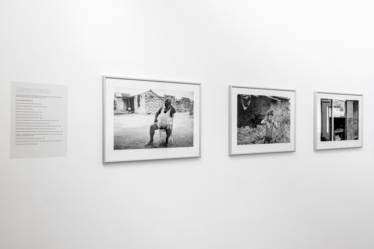 Installation photograph from the launch of Omar Badsha’s book ‘Seedtimes’ on A4’s top floor. On the left, Omar Badsha’s monochrome photographs ‘Induna Nkonyane, Amouti, Kwazulu-Natal’, ‘Young woman repairing home, Inanda, Kwazulu-Natal’ and ‘Watch repair shop, Inanda, Kwazulu-Natal’ are mounted on the wall.
